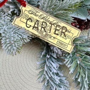 May include: Gold-coloured ticket ornament with the text "The Polar Express Round Trip" and the number "N*0001225". The ticket is decorated with rhinestones.