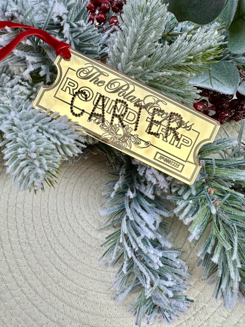 May include: Gold-coloured ticket ornament with the text "The Polar Express Round Trip" and the number "N*0001225". The ticket is decorated with rhinestones.