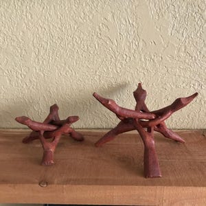 May include: Two reddish-brown wooden display stands with a tripod base design. Each stand features three interlocking carved wooden pieces that form a stable structure for holding spherical objects or bowls, showcasing a natural wood grain texture.