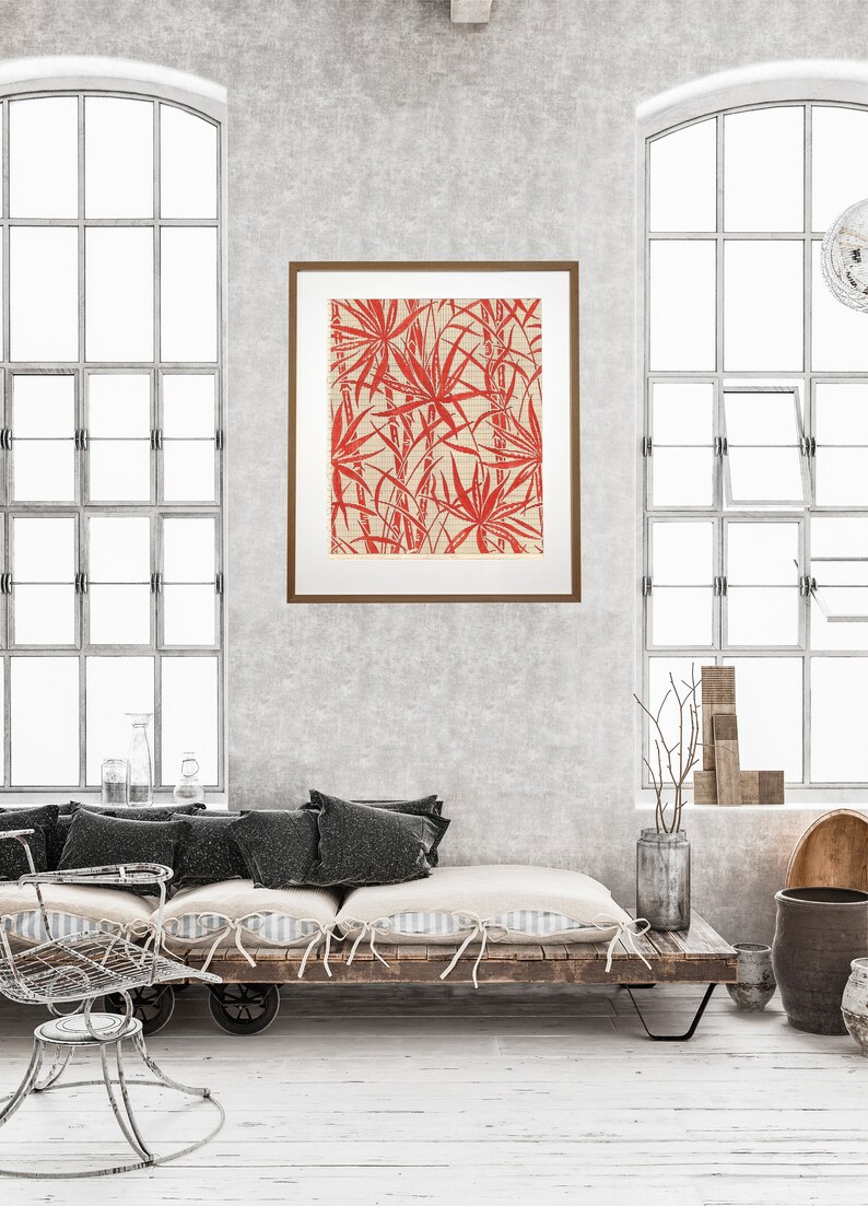 May include: A framed print of a red and white botanical illustration of palm leaves. The print is hanging on a gray wall above a wooden bench with black cushions.