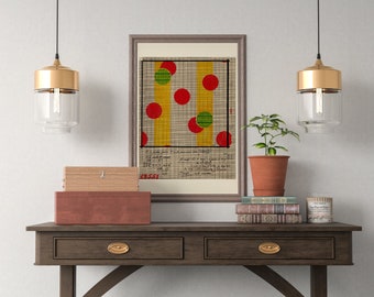 May include: A framed print of a geometric design with red, green, and yellow circles on a grid background. The print is hanging on a wall above a wooden table with a wooden box, a potted plant, and a stack of books.