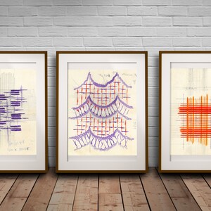 May include: Three framed abstract art prints with geometric patterns in shades of purple, red, and orange. The prints are on a white brick wall background.