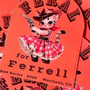 May include: Orange card featuring a cartoon kitten in a cowboy hat and dress, holding a gun. The text "for Ferrell" and "Red Rocks 2025 Morrison, CO" are also on the card.