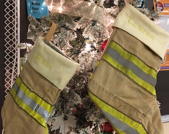 May include: Two firefighter-style stockings with yellow and silver reflective stripes hang on a flocked Christmas tree. The stockings are personalized with the names "Lauren" and "Matt".