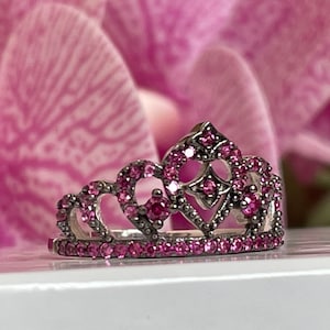 May include: A silver crown ring with pink gemstones. The crown is detailed with a heart shape in the center.