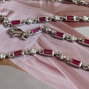 Peut inclure: Un bracelet en chaîne argent avec des pierres précieuses rectangulaires rouges et des pierres précieuses rondes claires alternées.