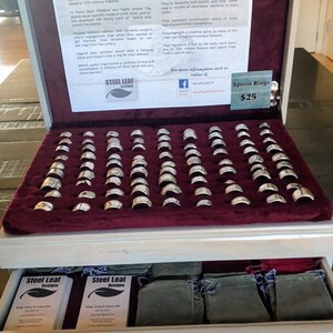 May include: A wooden box with a red velvet interior displaying a collection of silver spoon rings. The box has a drawer with small green pouches. The box has a sign that reads "Spoon Rings £25".