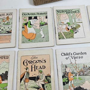 May include: A collection of vintage children's storybooks, including titles like "The Chocolate Man," "Old Mother Hubbard," and "Ali Baba." The books have colorful illustrations and are housed in a cardboard box labeled "Little Story Books."