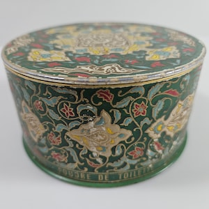 May include: A round green metal box with a floral design. The box has a silver lid and the words "Poudre de Toilette" are printed on the bottom.