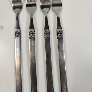 May include: Four stainless steel forks with a decorative band near the top of the handle. The tines are evenly spaced. The handles have a brushed finish. The forks are arranged vertically.