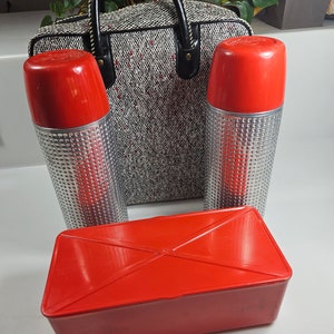 May include: A vintage picnic set with two red and silver thermoses, a red rectangular lunch box, and a black and white tweed travel bag.