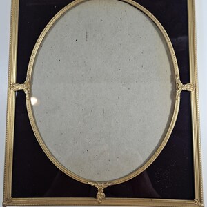May include: A gold-colored oval picture frame with a black velvet mat. The frame has ornate detailing and a decorative design.