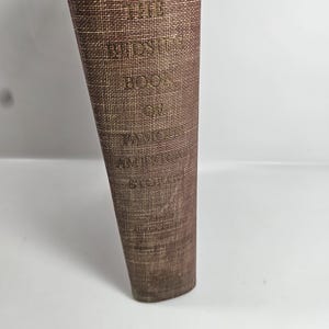 May include: A vintage book with a brown textured cover. The title "THE BEDSIDE BOOK OF" is printed in gold lettering. The book's spine is slightly worn, suggesting age and use. The book is a classic, likely for reading.