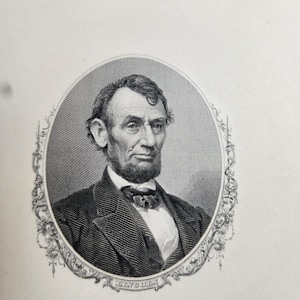 May include: An engraved portrait of Abraham Lincoln in a decorative oval frame. The black and white image shows Lincoln with a beard, bow tie, and suit. The name "LINCOLN" is printed at the bottom of the frame.