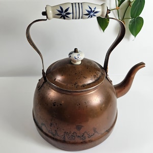 May include: A copper tea kettle with a blue and white porcelain handle and lid knob. The kettle has a worn, aged patina.