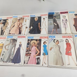May include: A collection of vintage Vogue Paris Original sewing pattern envelopes. The envelopes feature illustrations of women in stylish dresses, coats, and suits. The text "Vogue Paris Original" is prominently displayed on each envelope.