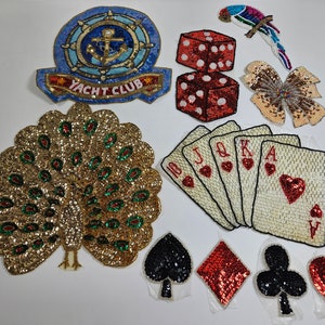 May include: Assortment of iron-on patches featuring a peacock, playing cards, dice, a butterfly, and a yacht club logo. The patches are all made of sequins and beads.