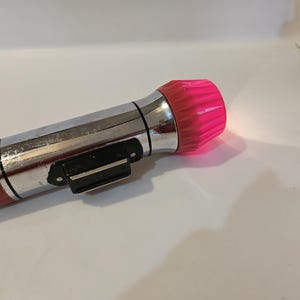 May include: A vintage silver flashlight with a red and white striped design and a pink plastic lens.