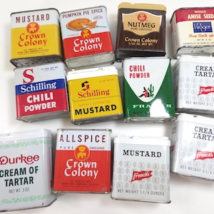 May include: A collection of twelve vintage metal spice tins featuring various brands including Crown Colony, Schilling, French's, and Durkee. The rectangular containers display colorful labels with text such as Mustard, Pumpkin Pie Spice, Nutmeg, Anise Seed, Chili Powder, Cream of Tartar, and Allspice, with net weights listed in ounces.