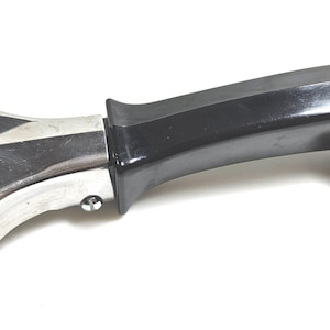 May include: A handheld ice scraper featuring a wide, flat, silver-colored metal blade attached to a curved, glossy black plastic handle. The handle includes a small metal loop at the end for hanging, and the blade is secured with two visible screws.