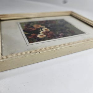 May include: A rectangular framed picture with a floral print. The frame is off-white with a textured, ridged design. The picture features a close-up of colorful flowers in shades of red, yellow, and orange.