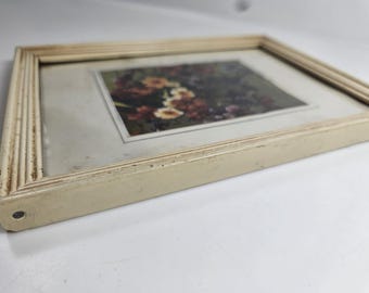 May include: A rectangular framed picture with a floral print. The frame is off-white with a textured, ridged design. The picture features a close-up of colorful flowers in shades of red, yellow, and orange.