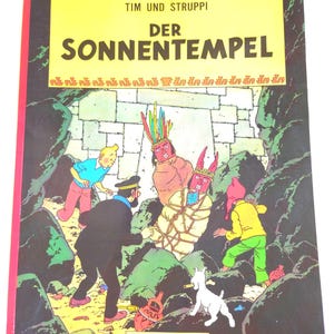 May include: A comic book titled Tim und Struppi Der Sonnentempel by Hergé, published by Carlsen Verlag. The cover features a colorful illustration of characters in a rocky cave, including a person bound in rope and two figures wearing masks.