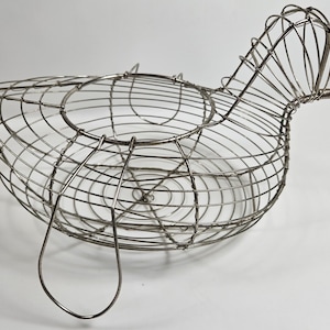 May include: A silver wire chicken-shaped basket with a handle. The basket is made of thin wire and has a rounded shape. It is designed to hold small items, such as fruit or eggs.