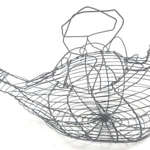 May include: A dark gray wire basket shaped like a bird, featuring a rounded body, a pointed tail, and a head with a beak. The structure is crafted from thin, interconnected metal wires forming a grid pattern, creating an open, hollow container.