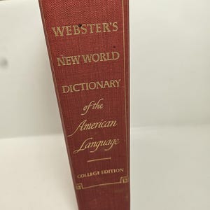 May include: A maroon-colored book titled "Webster's New World Dictionary of the American Language." The book's cover features gold lettering and decorative corner designs. The words "College Edition" and "World" are also visible.