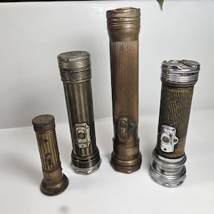 May include: Four vintage flashlights of varying sizes and designs. The flashlights are made of metal, with brass and silver tones. Each flashlight has a different pattern and switch design, showcasing a range of antique lighting technology.