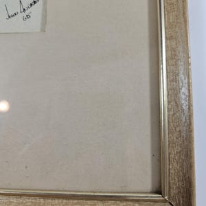 May include: A framed artwork with a light brown wooden frame and a white mat. The artwork is signed "John Anderson 60" in the top left corner.