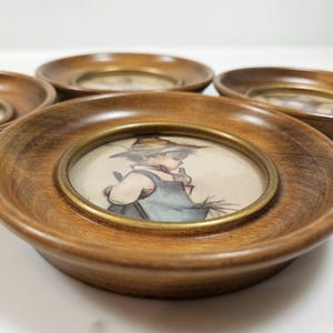 May include: Set of four vintage wooden coasters with a round, brass-toned inner ring. Each coaster features a small, framed illustration of a child in a straw hat. The wood has a warm, medium brown tone.