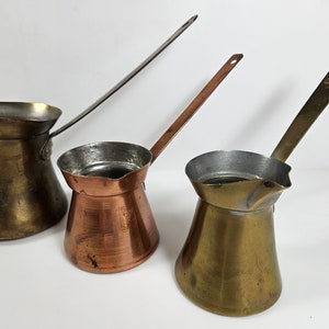 May include: Three vintage Turkish coffee pots, one with a copper body and two with brass bodies. The pots have long handles and are made of metal.