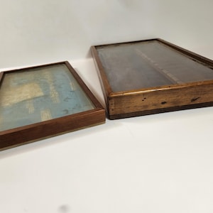 May include: Two rectangular wooden display cases with glass tops. The cases have a dark brown finish and are of different sizes. The smaller case is on the left, and the larger case is on the right. The glass tops are clear, and the interiors are visible.