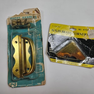 May include: Two packages of brass hardware. The first package contains a brass chest handle with screws. The second package contains four solid brass corners with screws. The packages are both yellow and black with white text.