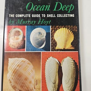 May include: A vintage book titled "Jewels from the Ocean Deep" with the subtitle "The Complete Guide to Shell Collecting by Murray Hoyt." The cover features a black background with green and white text and images of various seashells.