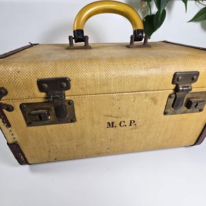 May include: A vintage yellow and brown suitcase with a yellow plastic handle and metal clasps. The suitcase has the initials "M.C.P." printed on the front.