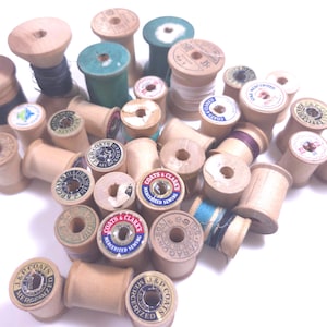 May include: A collection of vintage wooden sewing thread spools in various sizes, featuring natural wood finishes and some painted green ends. Many spools have paper labels with text including J. & P. Coats, Coats & Clark, and Paragon.