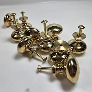 May include: A collection of polished brass cabinet knobs with screw attachments. The knobs have a rounded, oval shape and a shiny, reflective surface. The hardware is suitable for furniture restoration or new construction.
