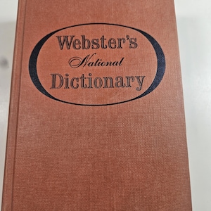 May include: A vintage dictionary with a textured, reddish-brown cover. The title "Webster's National Dictionary" is displayed in a black oval with elegant script lettering. The book appears to be in good condition.