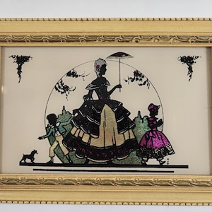 May include: A framed silhouette artwork depicting a woman in a long dress holding an umbrella, walking with two children and a small dog. The artwork is set against a white background with a circular design and green foliage.