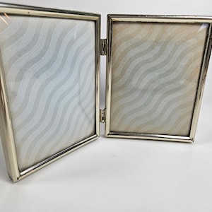 May include: A silver-toned double picture frame with a wavy pattern on the back of the frames.