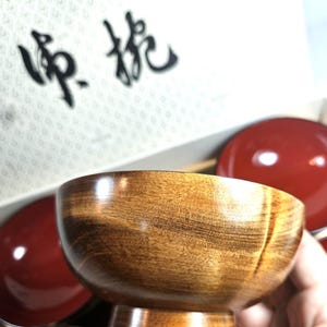 May include: A round wooden bowl with a natural brown wood grain finish on the exterior and a smooth, glossy red interior. The bowl features a raised circular base and is presented in a white box with black Chinese characters printed on the lid.