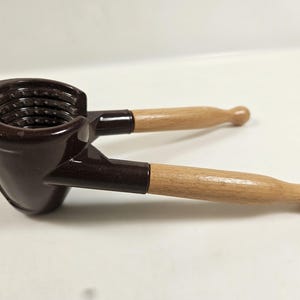 May include: A brown nutcracker with wooden handles. The nutcracker has a dark brown, glossy finish on the cracking mechanism and the connecting arms. The handles are made of light-colored wood.