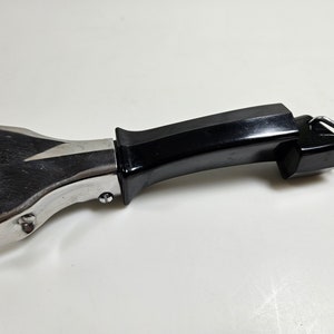 May include: A black and silver pot handle with a metal base and a black plastic handle. The handle has a metal clip to attach it to the pot.