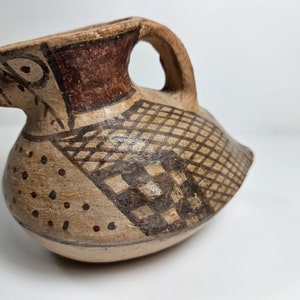 May include: A small, brown ceramic pitcher with a bird-shaped spout and handle. The pitcher is decorated with geometric patterns in black and brown paint.