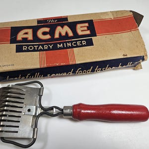 May include: A vintage red handled rotary meat grinder with a silver metal blade. The box reads "The Acme Rotary Mincer" and "1935 Am Gmco".