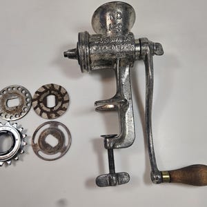 May include: An antique, silver-colored meat grinder with a wooden handle and several interchangeable grinding plates. The grinder is marked "No. 120" and "Enterprise Mfg. Co. of PA, U.S.A."
