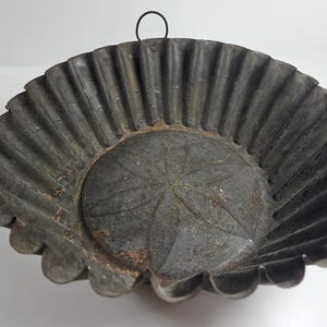 May include: A vintage metal pie pan with a fluted edge and a star-shaped design in the center. The pan has a black finish and a wire handle.